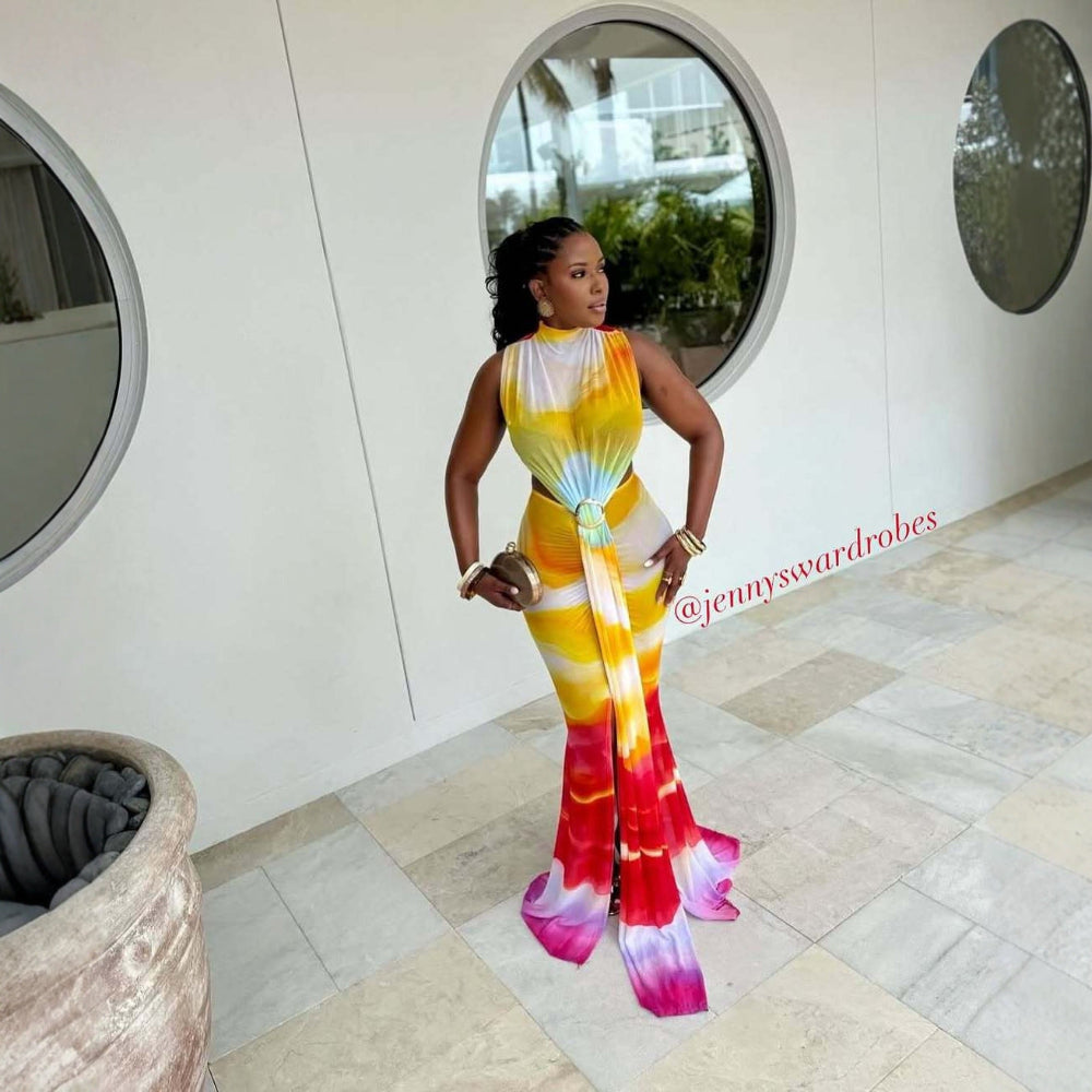 "Woman in a vibrant yellow, orange, and pink tie-dye gradient maxi dress with high slit and halter neckline, posing in a modern indoor space with circular mirrors"