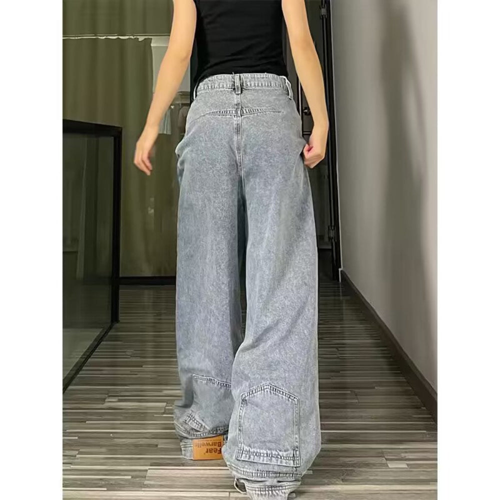 Woman modeling light-wash blue wide-leg baggy jeans from the back, paired with a black crop top, standing in an indoor hallway with wooden flooring.