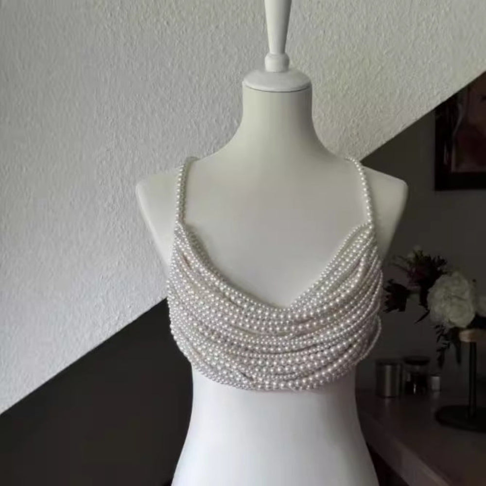 Front view of a white mannequin displaying a luxurious multi-layered pearl crop top. The top features dozens of delicate white pearl strands layered horizontally across the bust and torso, with pearl straps over the shoulders, creating an elegant, statement-making halter-style design.