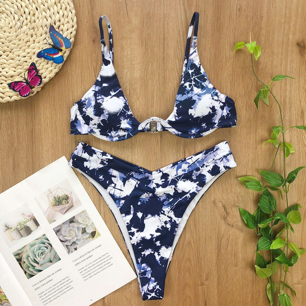 Blue and white floral bikini set on a wooden surface with a magazine and butterfly decorations.