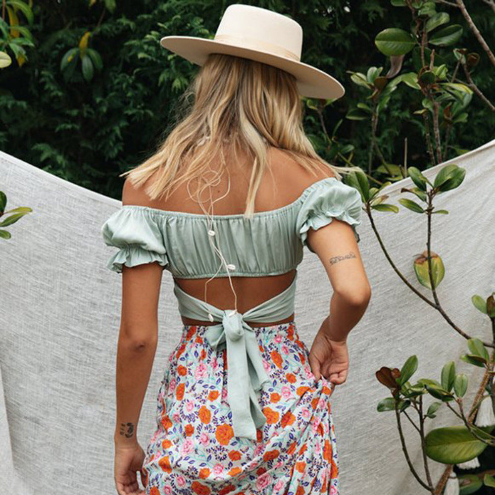 Sage green off-shoulder ruched crop top with puff sleeves and tie-back closure, paired with a floral skirt, worn by a model from the back.