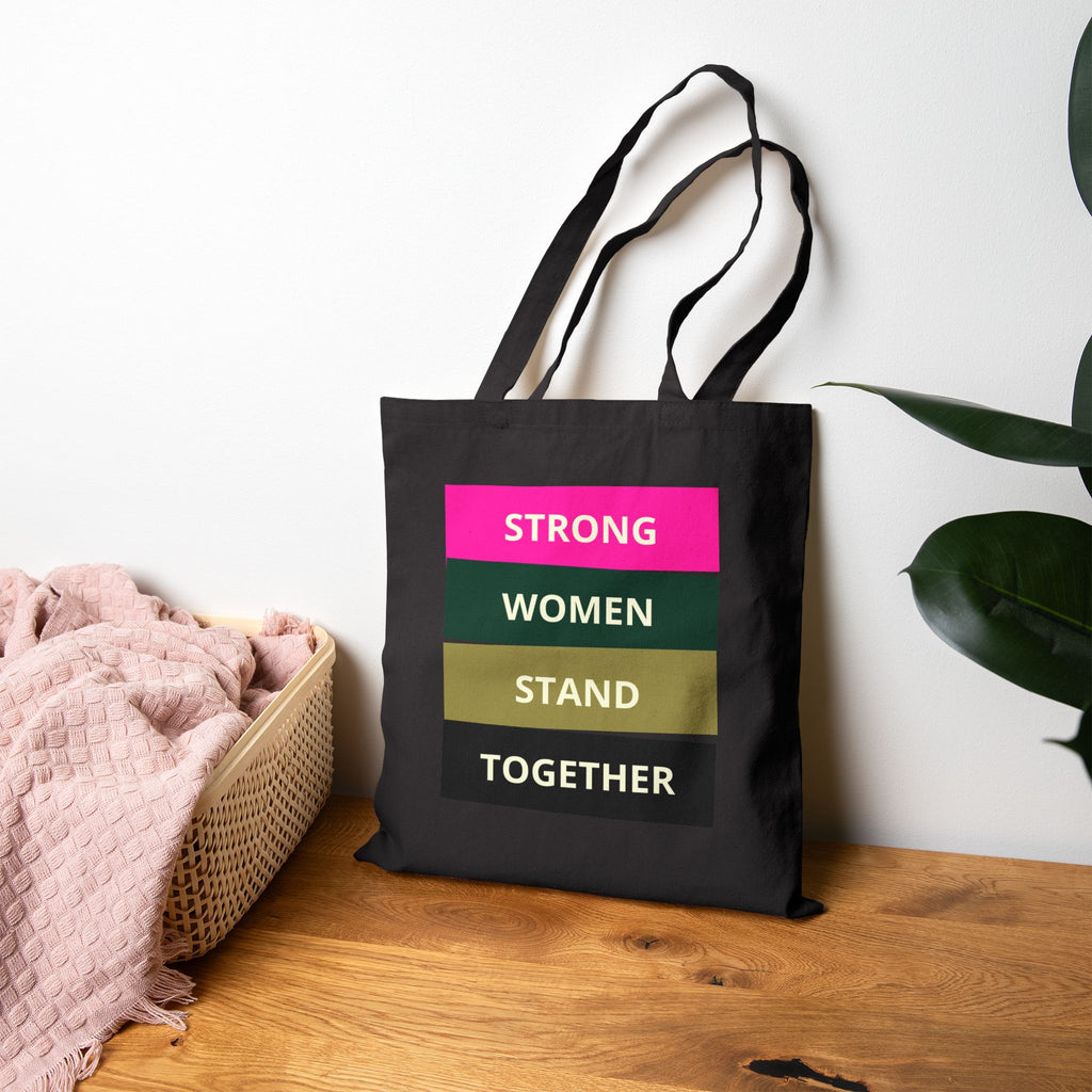 Black tote bag with motivational quote on a wooden surface with a plant in the background