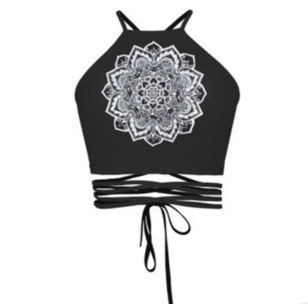Black halter crop top with large white mandala graphic print and multi-strap tie-back detail, shown flat lay on white background.