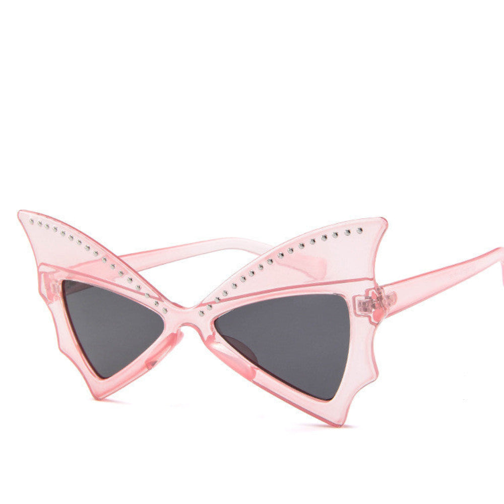 Pink translucent batwing sunglasses with rhinestone brow line and dark lenses, product photo on a white background.