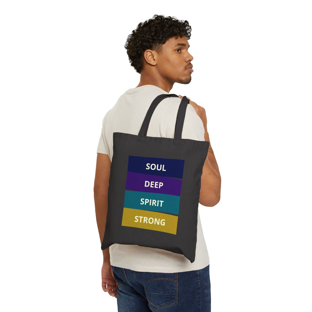 Man with curly hair wearing a black canvas tote bag with "SOUL DEEP SPIRIT STRONG" motivational quote in colorful stacked blocks, shown from back three-quarter view against white background.
