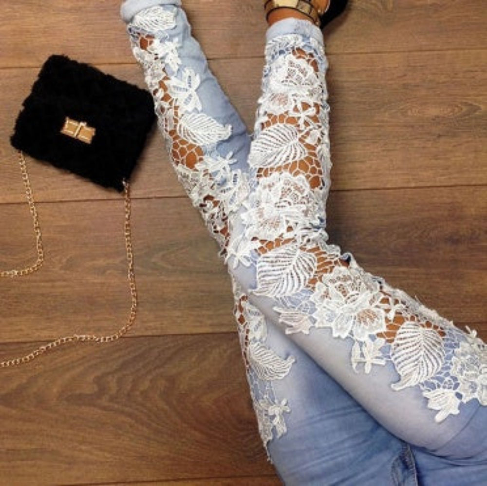 Top-down view of woman’s legs in light blue skinny jeans featuring intricate white floral lace panels, posed on a wooden floor next to a black furry handbag with gold chain. Stylish fashion product photography for Boutique Jolie.
