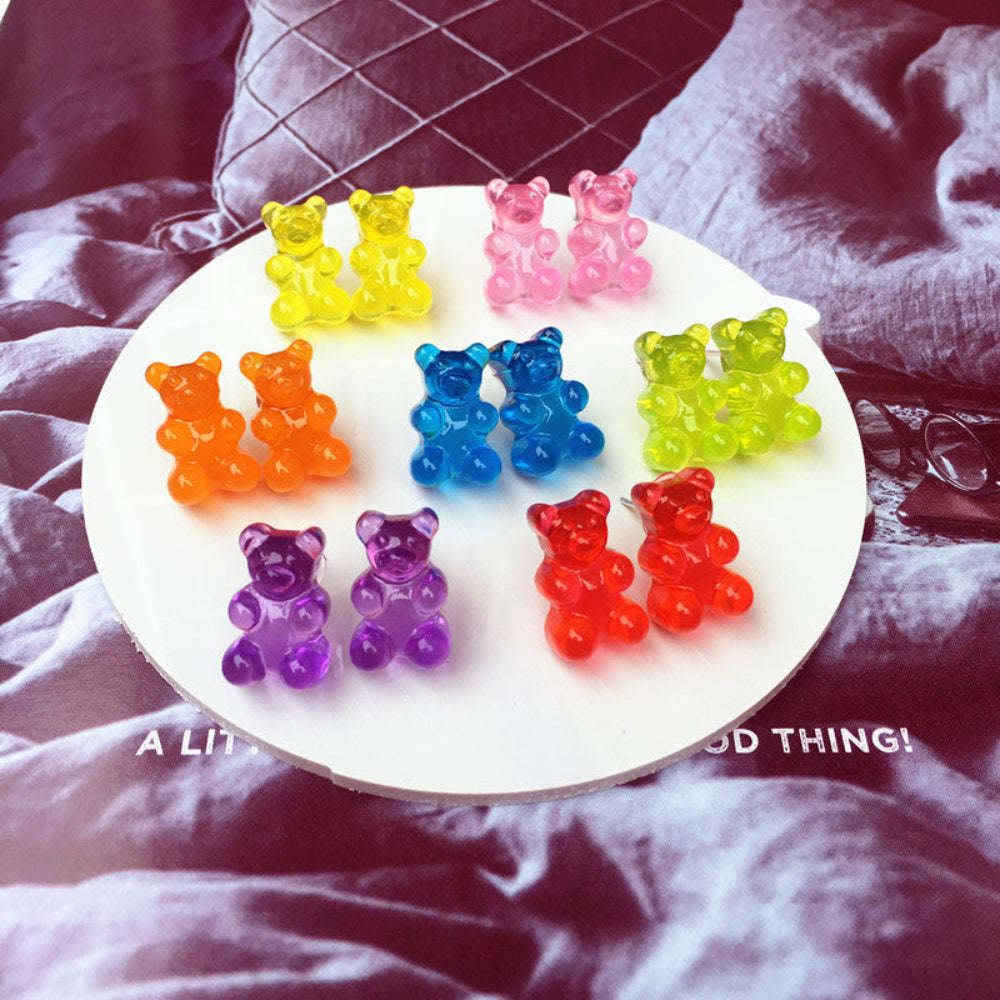 Assorted rainbow gummy bear earrings featuring translucent jelly bear studs in yellow, pink, lime green, orange, blue, purple, and red, displayed in pairs on white tray.