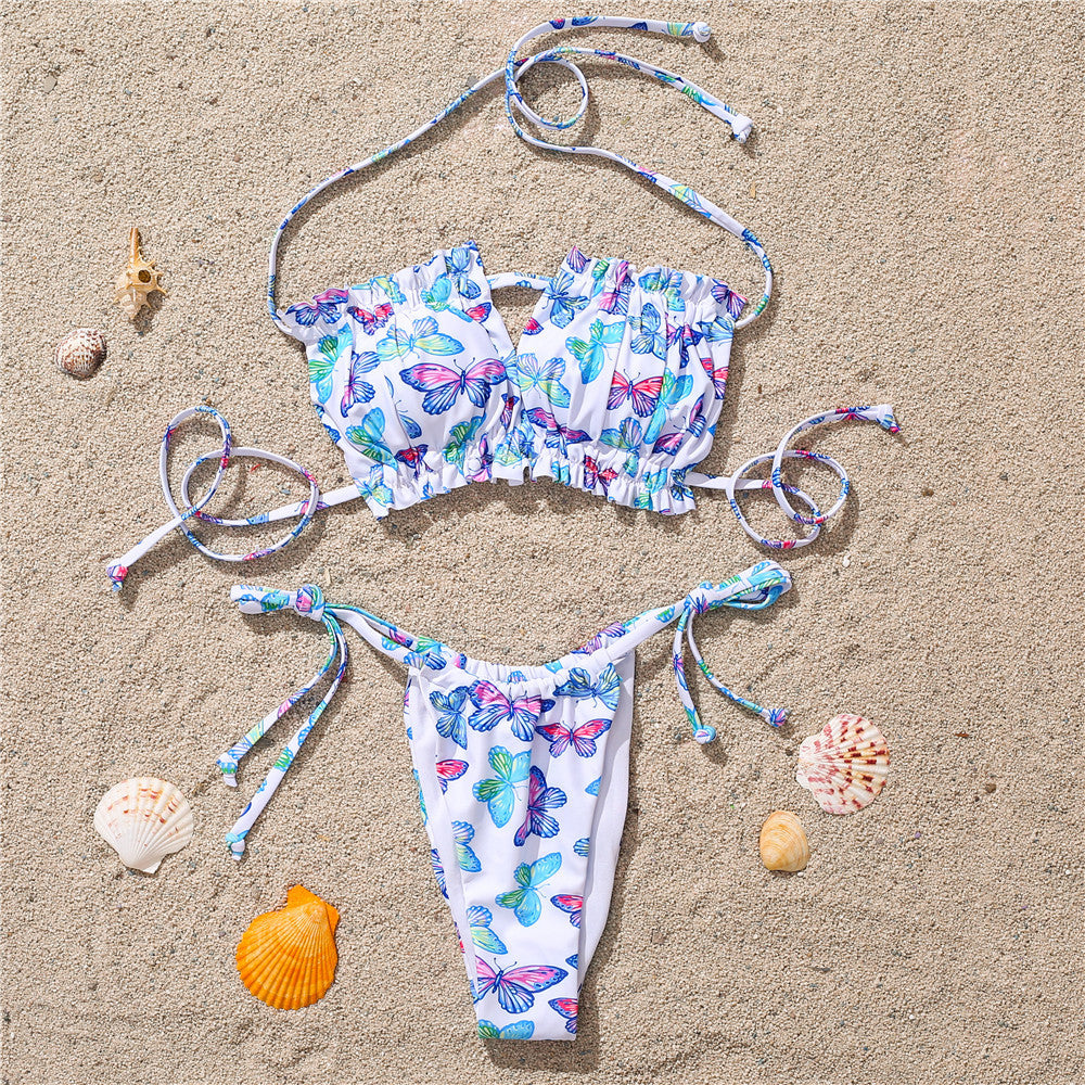 White colorful butterfly print bikini on sand – trendy ruffled swimwear set with ties, beach product flat lay.