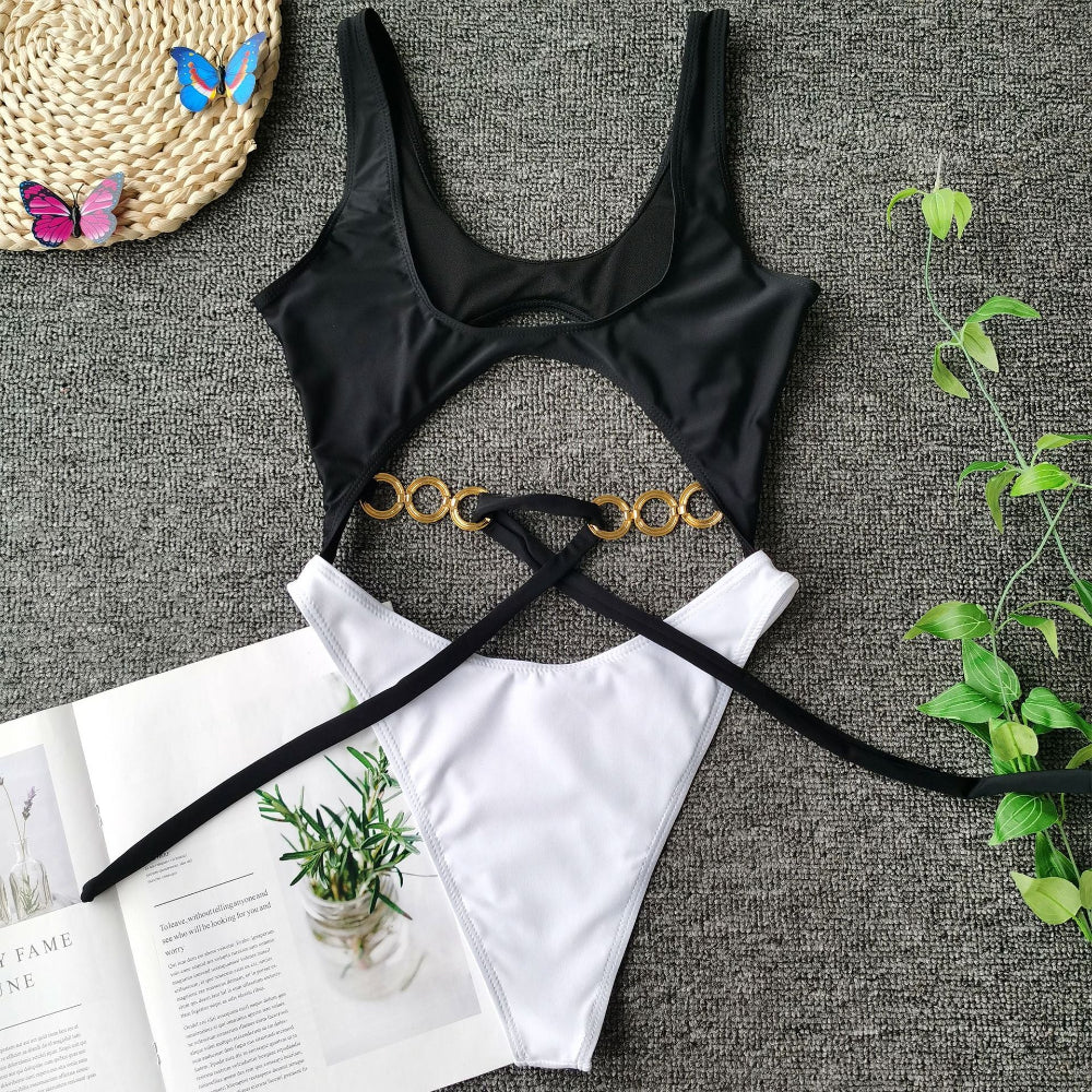 Black cutout one-piece swimsuit with gold ring detail and tie waist flat lay.