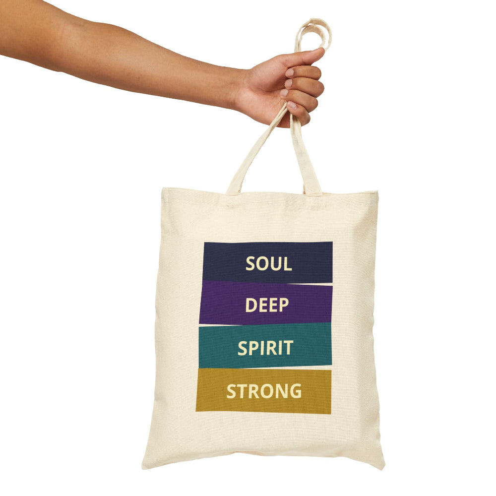 Natural canvas tote bag with "SOUL DEEP SPIRIT STRONG" motivational quote in colorful stacked blocks (navy, purple, teal, gold), held by hand against white background.