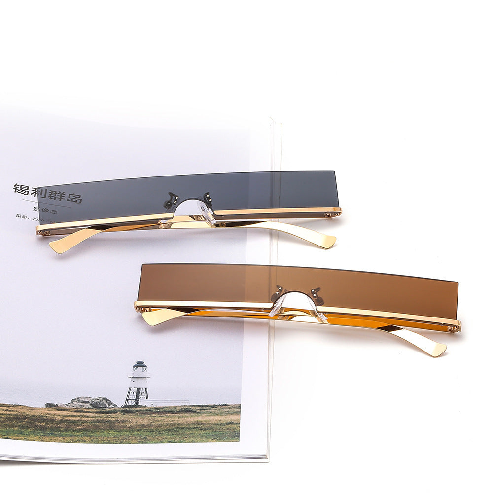 Rimless rectangular sunglasses in dark gray and brown with gold temples, styled on a magazine.