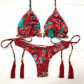 Red and green floral bikini set with tassels on a white wooden background