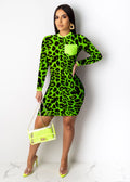 "Woman in a neon green leopard print long-sleeve mini dress with lime green chest pocket, holding a matching neon green transparent handbag and yellow heels on a white background"