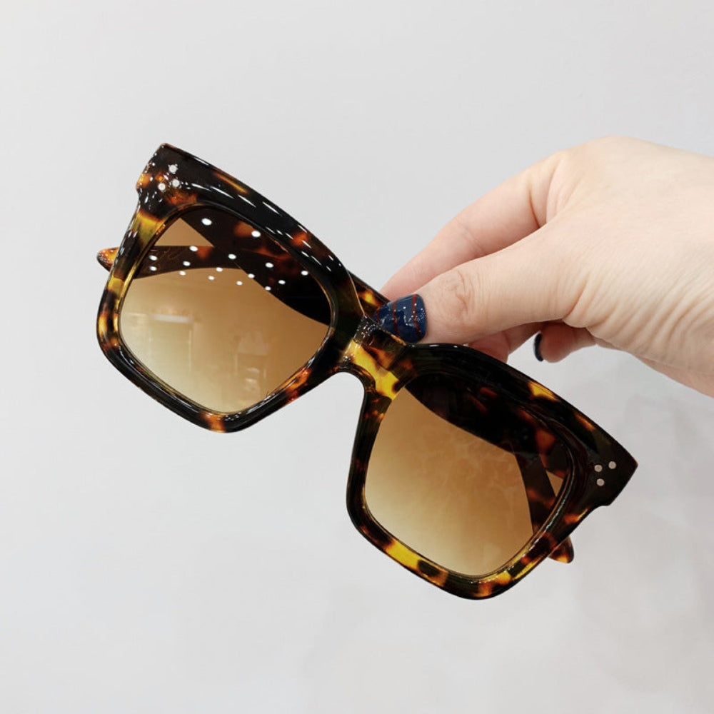 Tortoiseshell oversized square sunglasses with brown gradient lenses and crystal temple accents, held in hand.