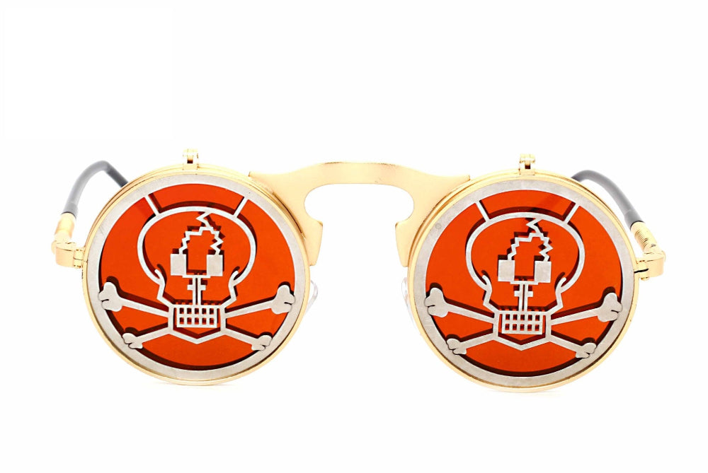 Gold flip-up steampunk sunglasses with orange lenses and silver skull-and-crossbones covers, front product photo on a white background.