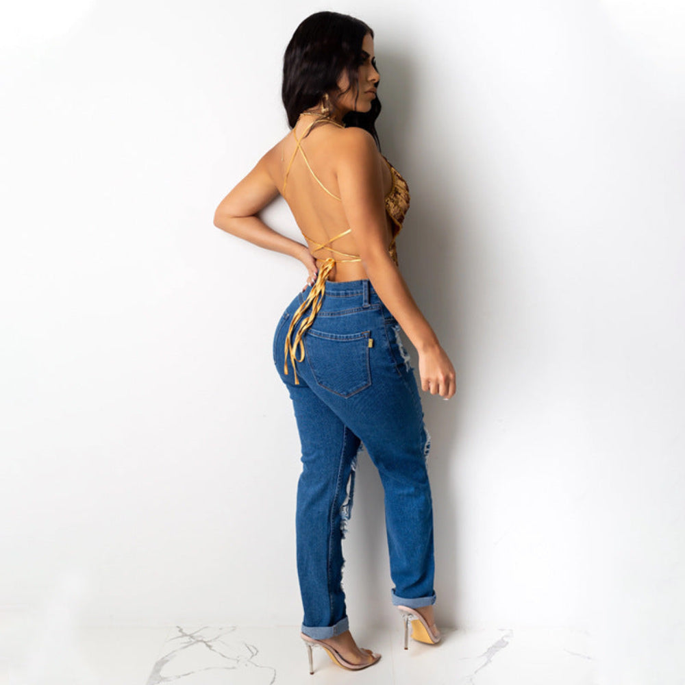 Gold sequin butterfly cut-out crop top with crisscross tie-back, paired with blue distressed ripped jeans, shown on a model from the back.