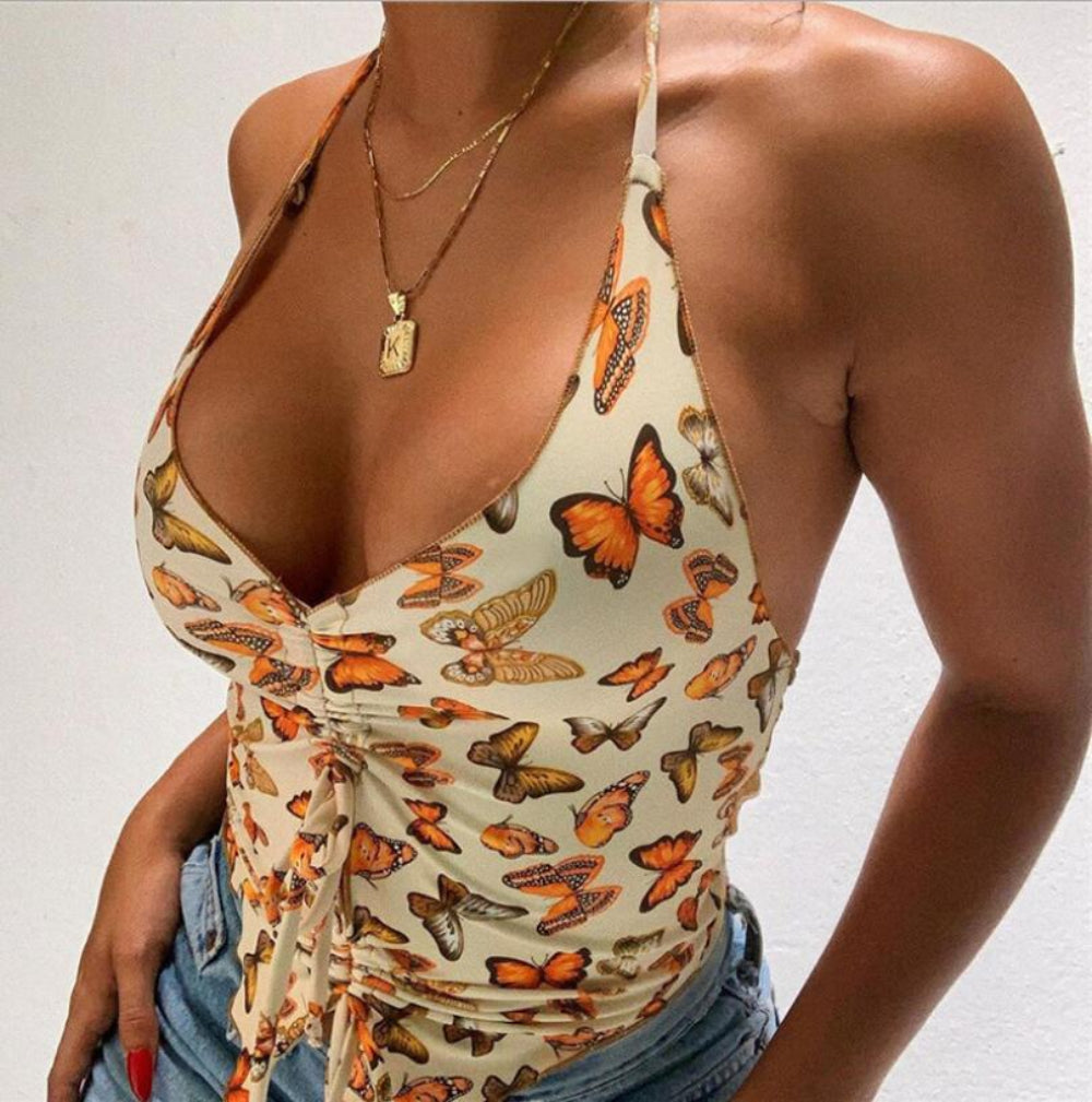 Cream butterfly print halter crop top with deep plunge V-neck, front tie knot detail, and ruched side, paired with denim jeans.