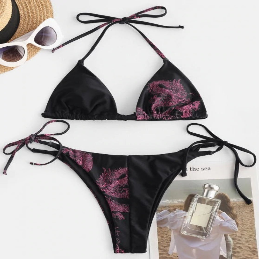 Black bikini with pink floral patterns, sunglasses, and a bottle of perfume on a white background.