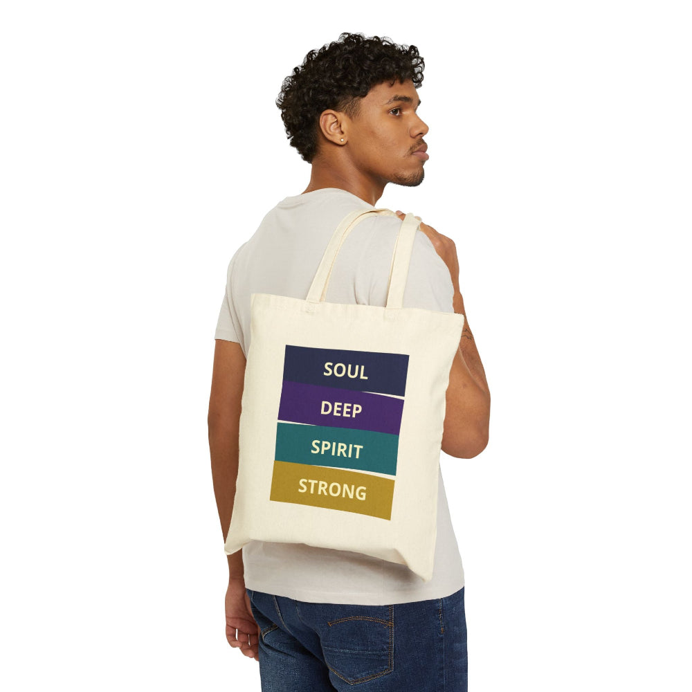 Man with curly hair wearing a natural canvas tote bag with "SOUL DEEP SPIRIT STRONG" motivational quote in colorful stacked blocks, shown from back three-quarter view against white background.