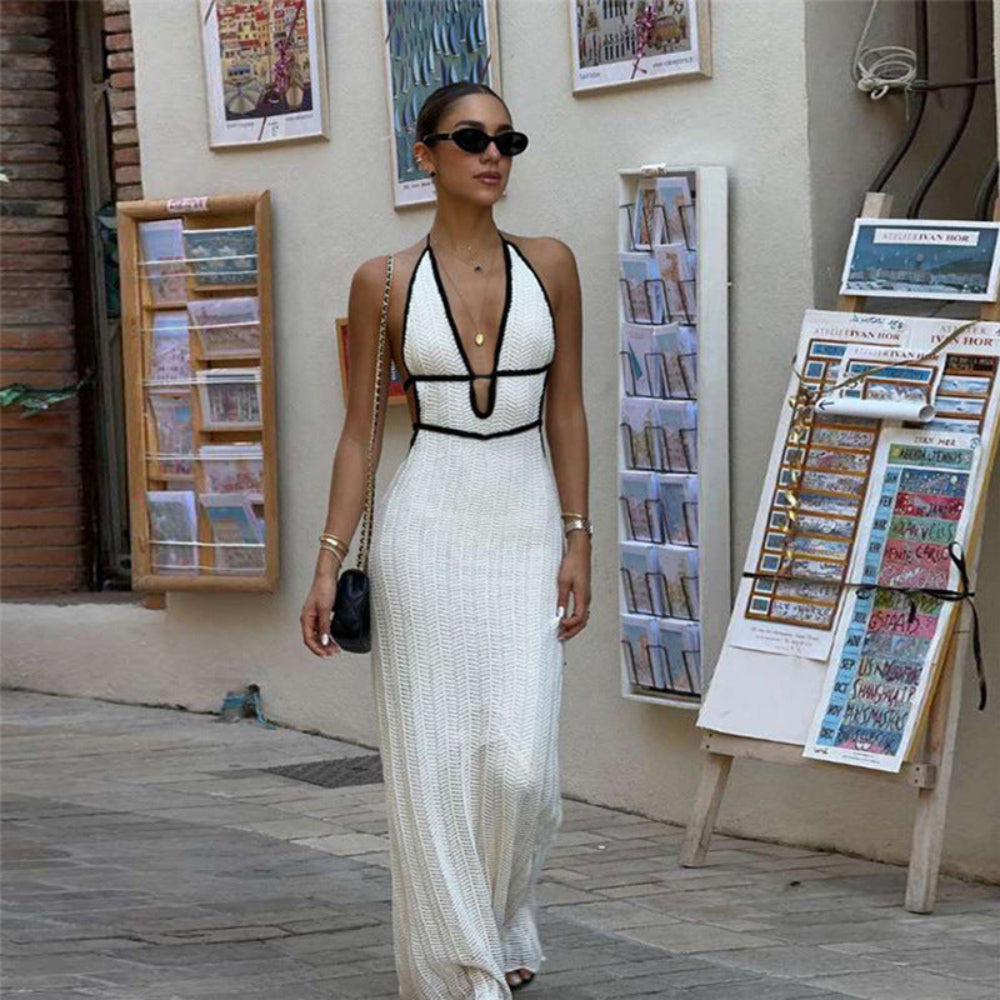Model wearing white ribbed knit halter maxi dress with black trim and cutout details, accessorized with sunglasses and handbag on city street.