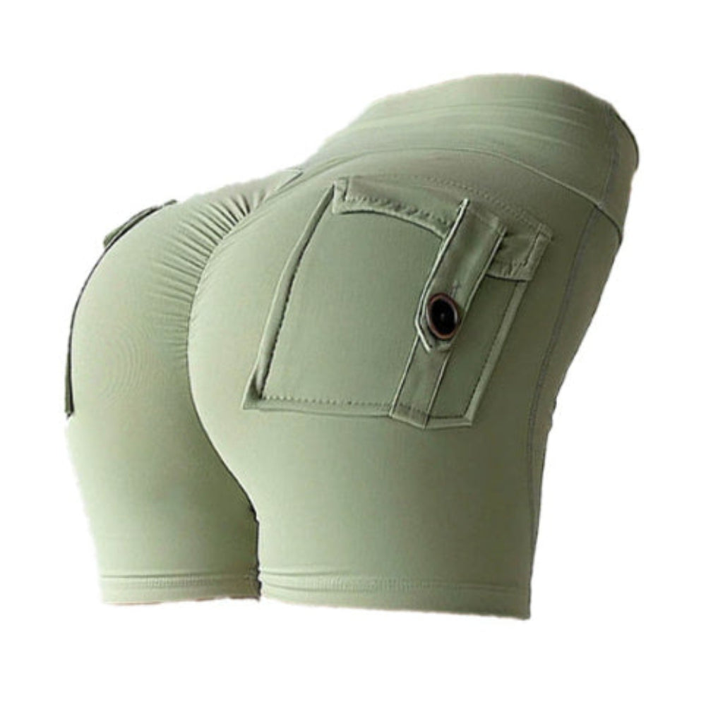 Woman modeling light green high-waisted athletic shorts with a large back cargo pocket and button detail, shown from a rear three-quarter view against a clean white studio background.