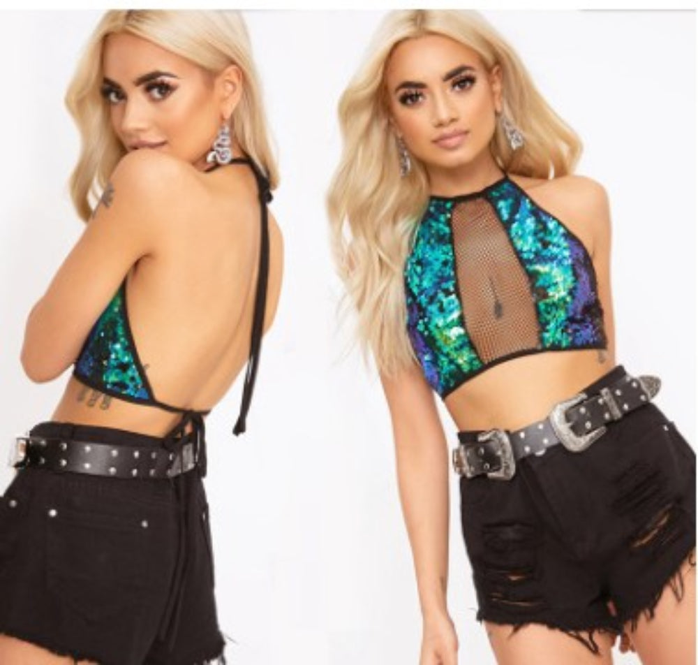 Two-panel view of a woman with long wavy blonde hair modeling a vibrant iridescent sequin halter crop top in blue, green, and purple tones with a sheer black fishnet mesh center panel. The back view shows the open-back design with tie straps. Styled with black distressed denim shorts and a wide black statement belt with large silver buckles.