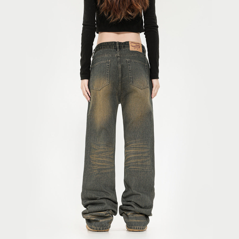 Back view of a model wearing dark grey wide-leg baggy jeans with heavy fading and whiskering on the thighs and knees. The jeans feature a relaxed, oversized fit that stacks at the ankles, classic five-pocket styling, and a brown leather brand patch on the waistband. Paired with a black long-sleeve crop top.