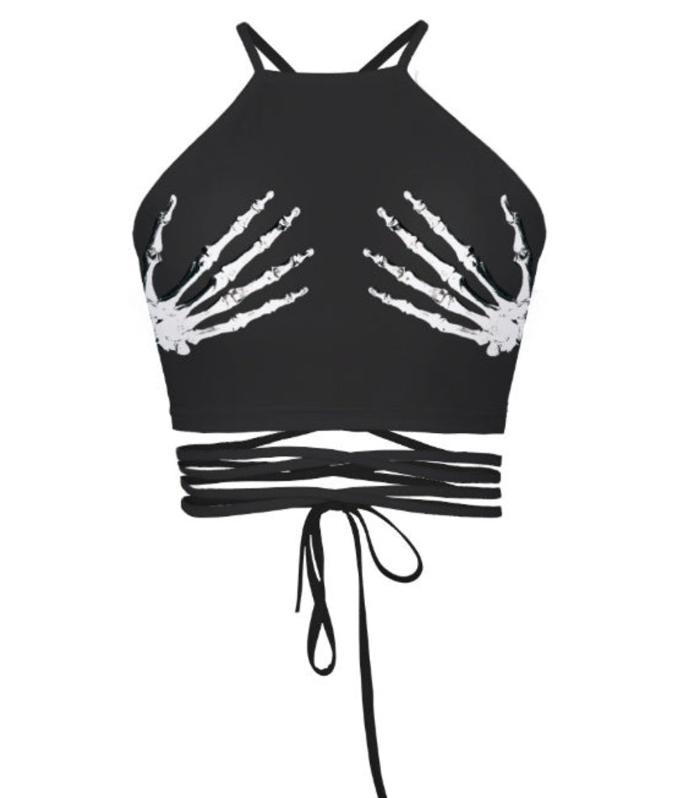 Black halter crop top with white skeleton hand graphics on the chest and multi-strap tie-back detail, shown flat lay on white background.