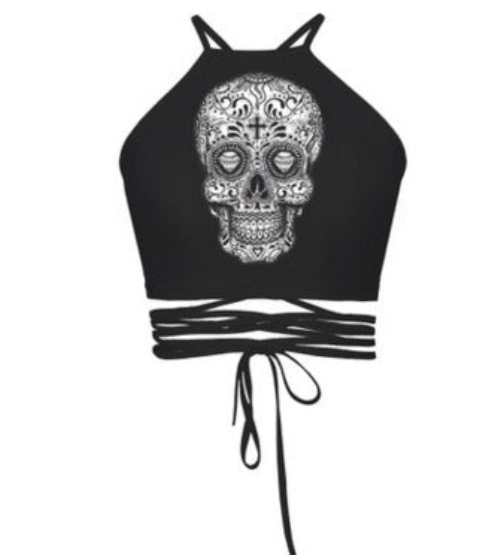 Black halter crop top with large white ornate sugar skull graphic print and multi-strap tie-back detail, shown flat lay on white background.
