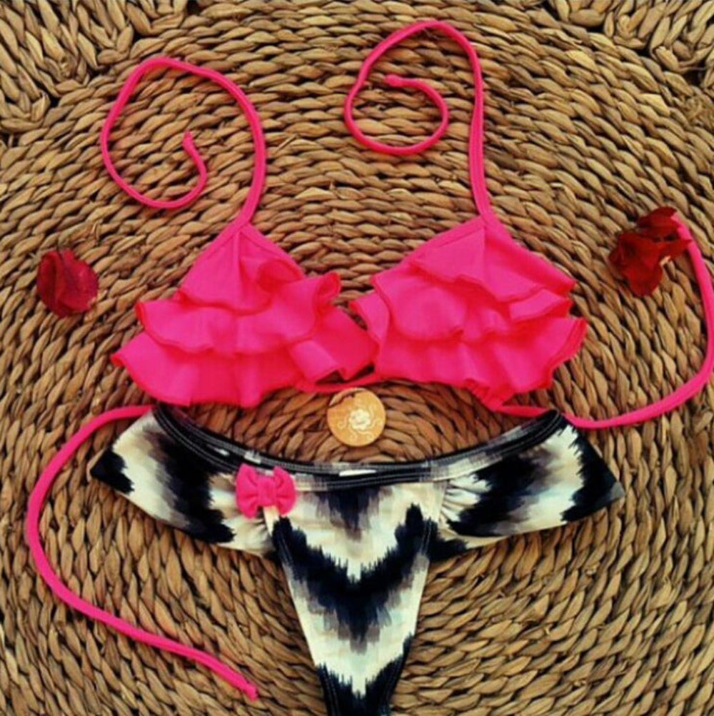 Pink ruffled bikini top with black white tie-dye bikini bottom flat lay on woven mat.