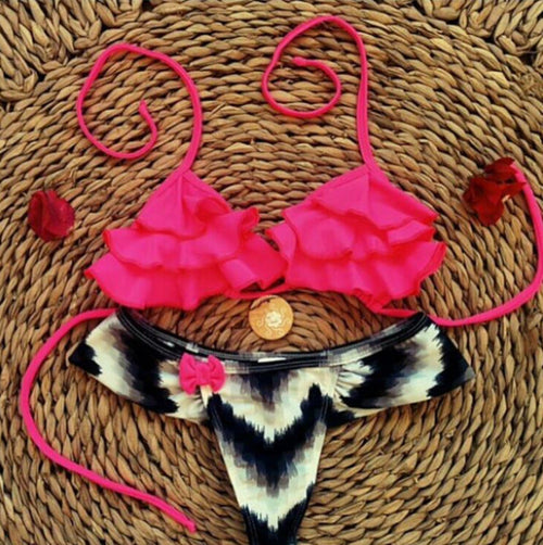 Pink ruffled bikini top with black white tie-dye bikini bottom flat lay on woven mat.