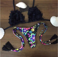 Black ruffled bikini top with colorful floral print tie-side bikini bottom with tassels flat lay.