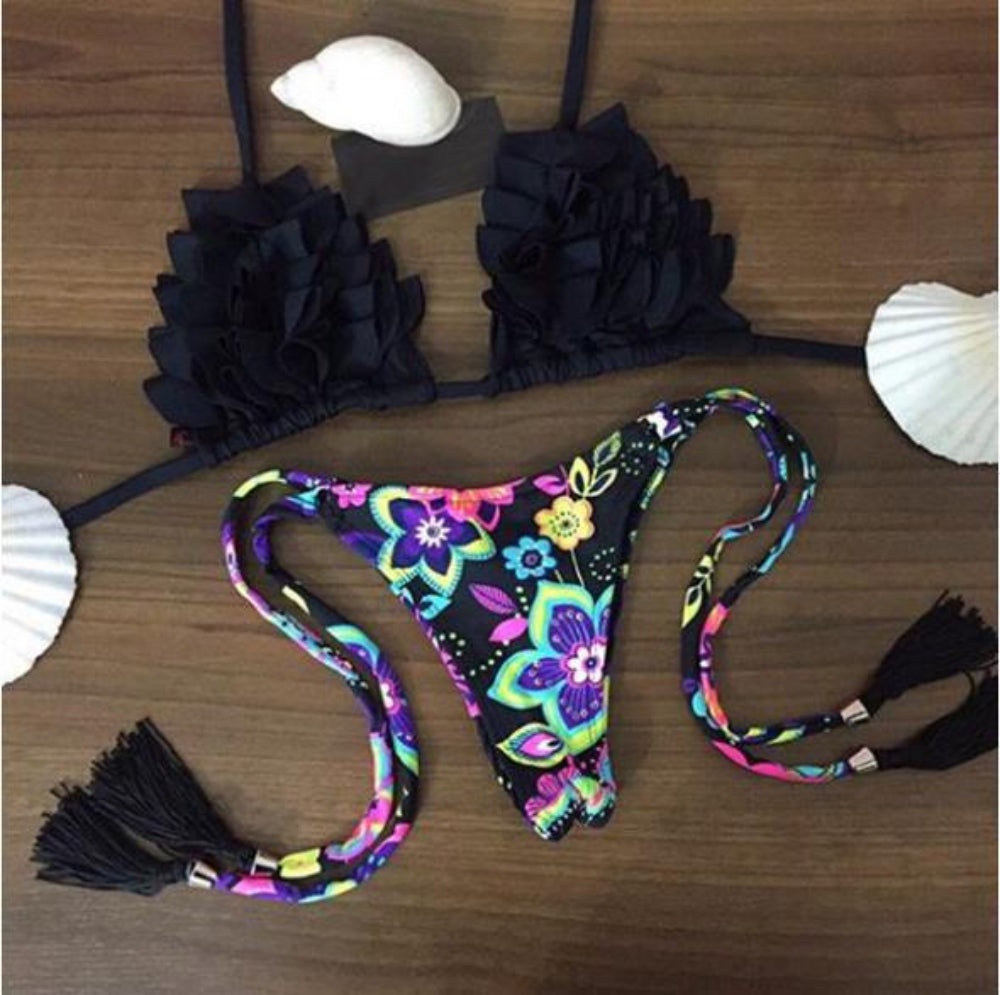 Black ruffled bikini top with colorful floral print tie-side bikini bottom with tassels flat lay.