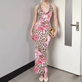 Model wearing a striking long form-fitting dress featuring a classic leopard print base with vibrant pink and magenta floral overlays. Sleeveless style with a flattering neckline, posed confidently in a bright room with a white door in the background.