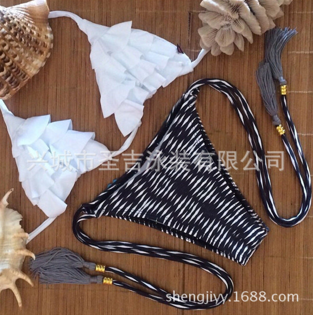 White ruffled bikini top with black and white striped tie-side bikini bottom with tassels flat lay.