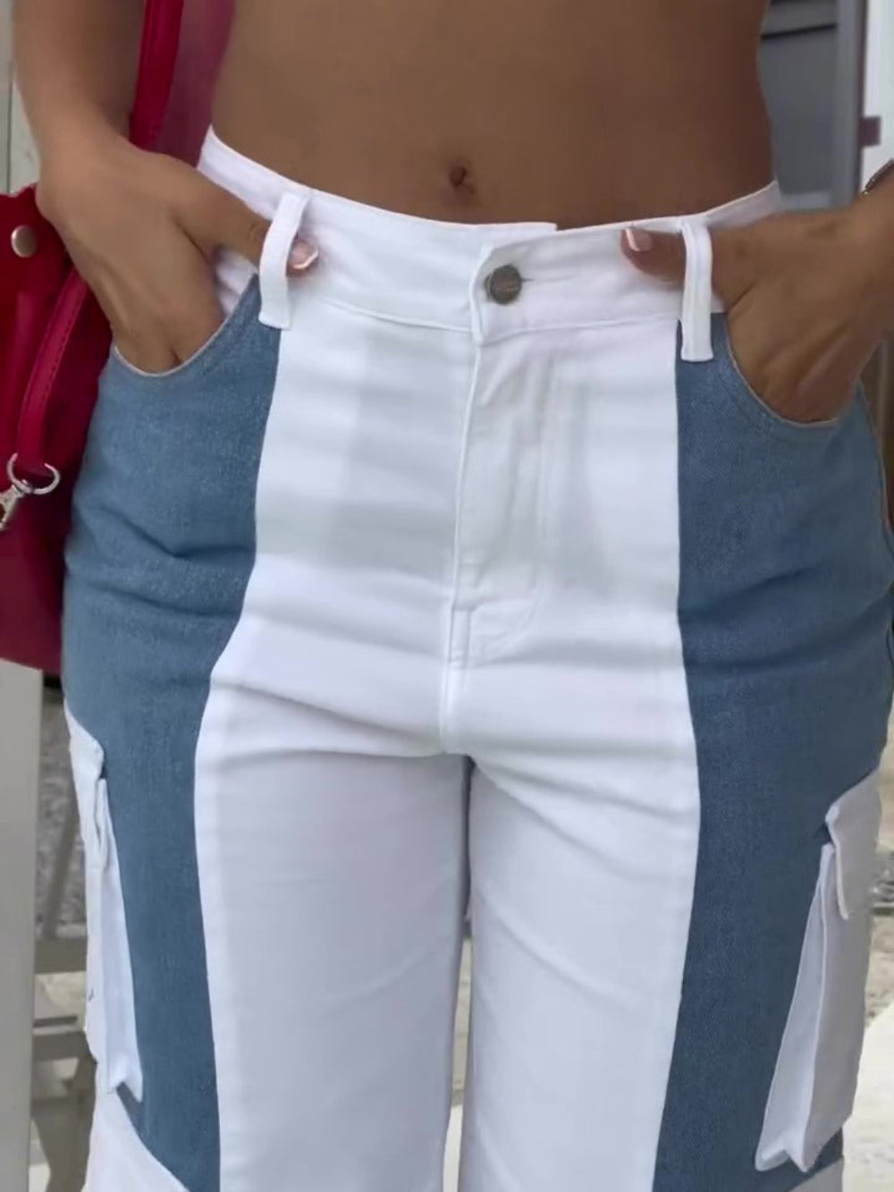 Woman modeling stylish color-blocked white and blue high-waisted cargo pants with multiple pockets and side panels, hands in pockets. Trendy casual fashion shot for Boutique Jolie.