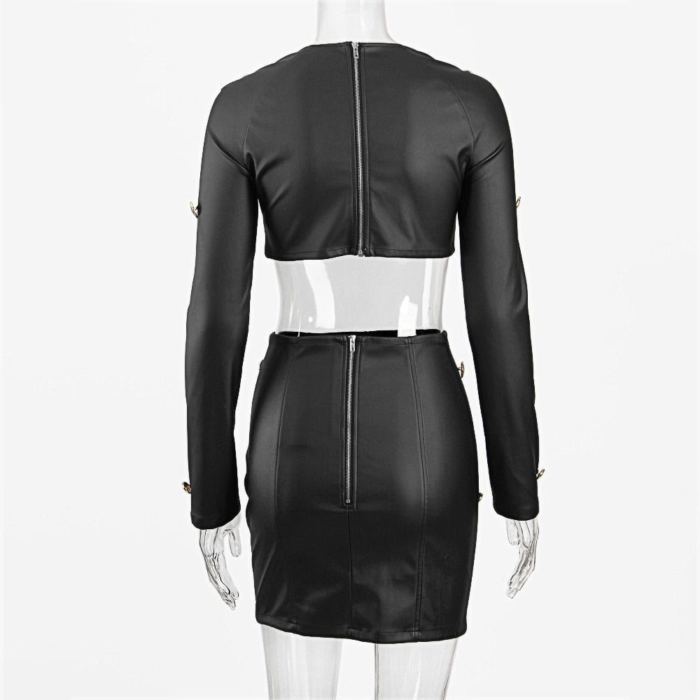 Rear view of a black faux leather two-piece outfit on a mannequin: cropped long-sleeve top and fitted mini skirt, both featuring gold button details and functional center-back zippers. Full product shot highlighting the structured silhouette on a plain white background.