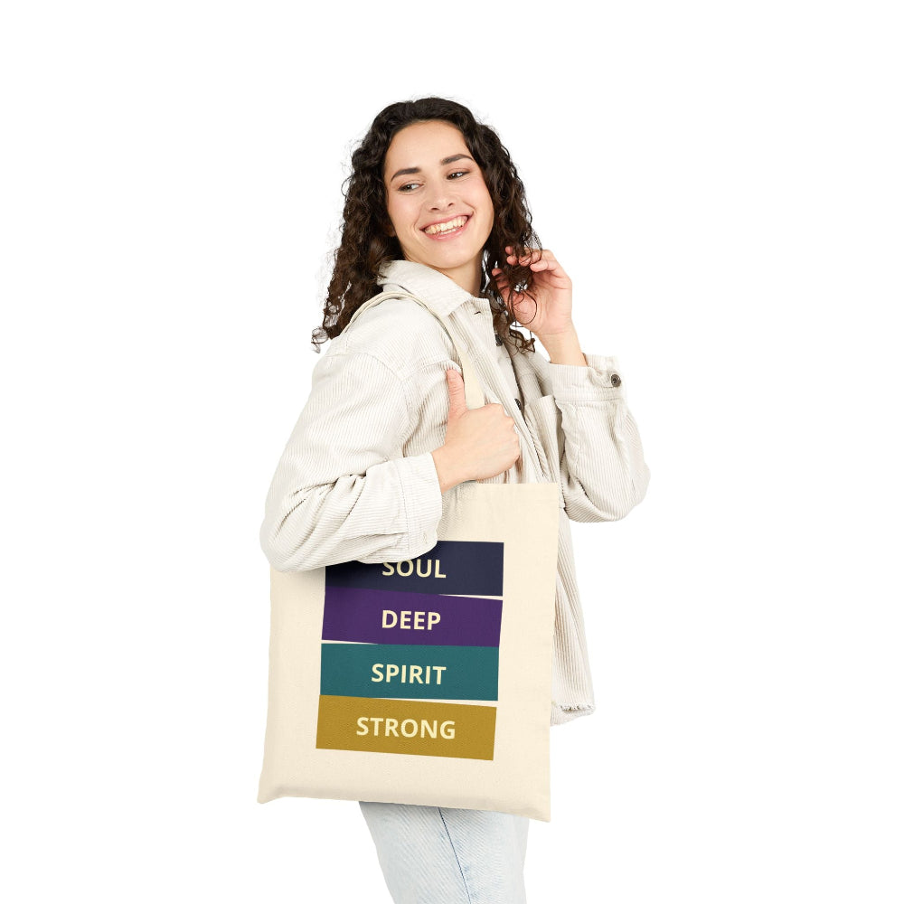 Smiling woman with curly hair carrying a natural canvas tote bag with "SOUL DEEP SPIRIT STRONG" motivational quote in colorful stacked blocks against white background.