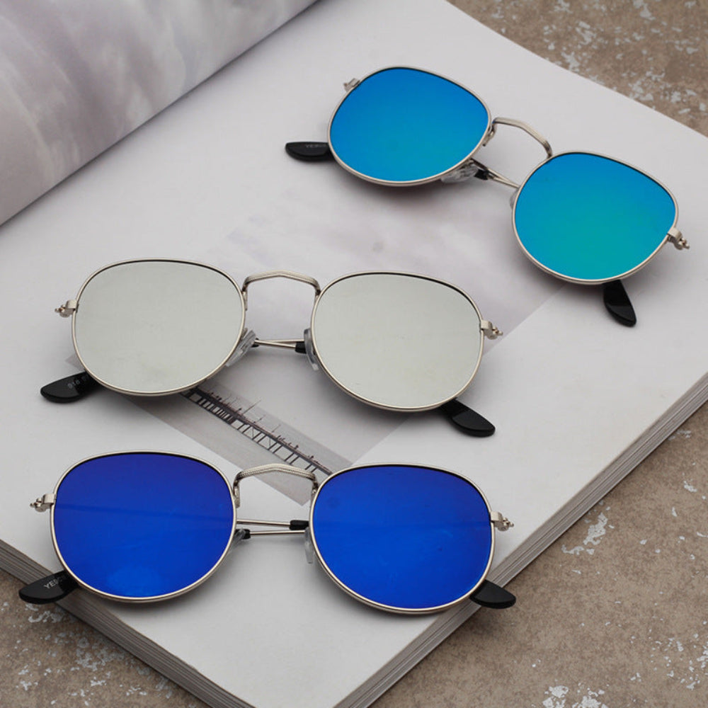 Three pairs of stylish silver metal oval sunglasses featuring vibrant blue mirrored lenses, turquoise blue mirrored lenses, and silver mirrored lenses, displayed on an open book