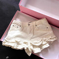 Cream-colored denim shorts with playful ruffled hems and front pockets, neatly displayed inside a pink gift box. Cute and feminine casual shorts product photography for Boutique Jolie.