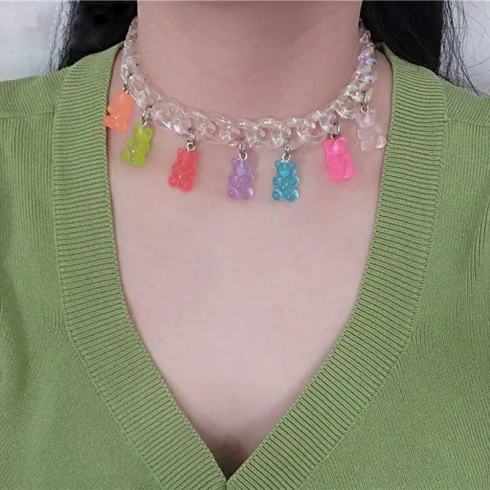Iridescent clear chunky chain choker necklace adorned with colorful translucent gummy bear charms in orange, green, red, purple, blue, and pink. Bold, playful statement piece shown worn on a model over a green top.