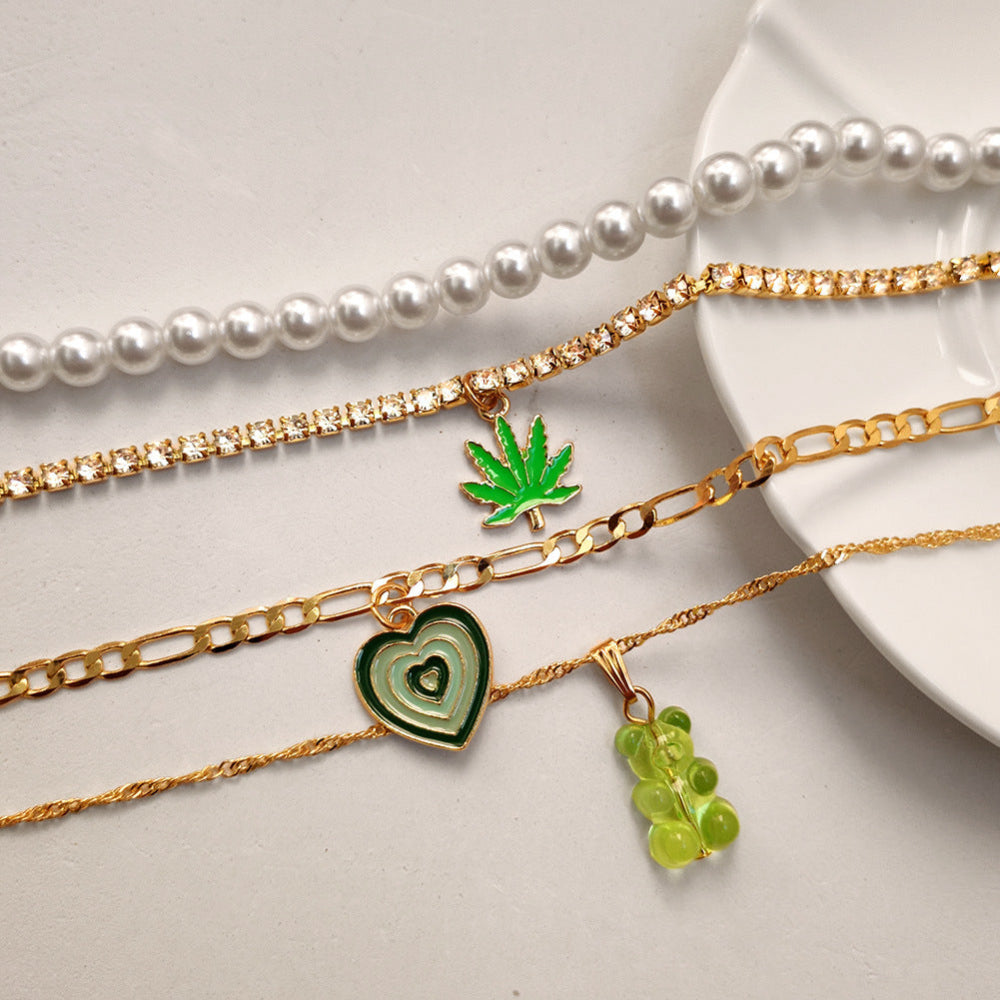 Gold pearl layered necklace set with green heart, leaf & gummy bear pendants – trendy statement jewelry collection on white background.
