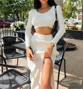 Woman wearing white ribbed long-sleeve crop top and high-slit midi skirt set, standing outdoors at cafe setting.