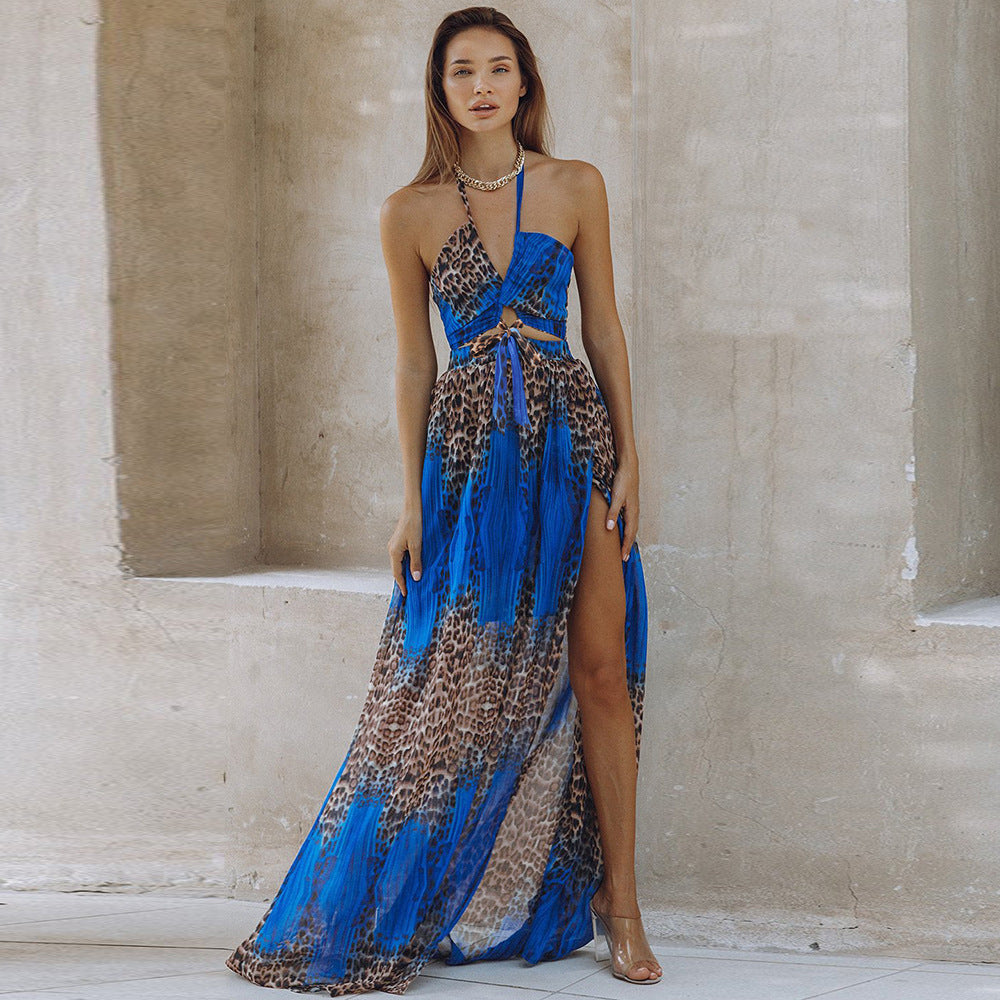 Woman modeling a striking blue and leopard print maxi dress with high side slit and tie detail, standing elegantly against a textured stone wall.