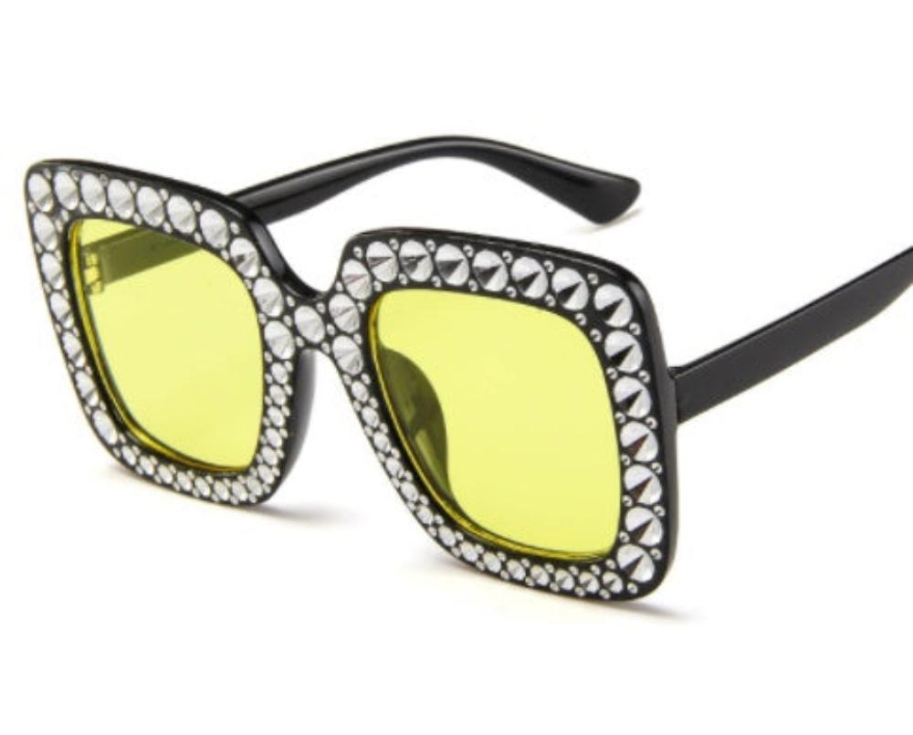 Black oversized square sunglasses with yellow lenses and crystal-studded frames, product photo on a white background.