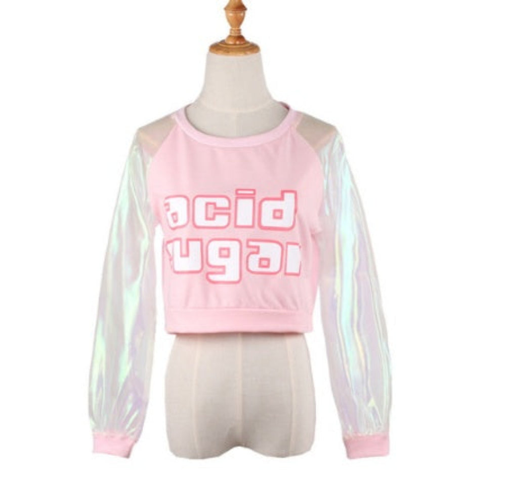 Pink cropped sweatshirt on a mannequin featuring bold acid sugar graphic text across the chest and sheer iridescent holographic long sleeves with pink cuffs. The trendy Y2K-style top has a relaxed fit and round neckline.