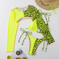 Neon green and black leopard print bikini set on a white surface with a straw hat and small plant.