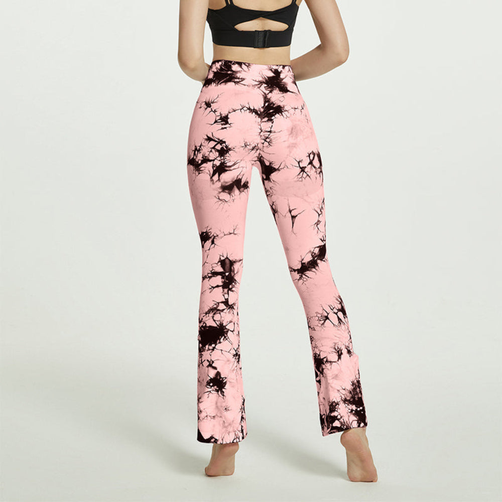 Woman modeling pink and black tie-dye high-waisted flared leggings, shown from the back while standing barefoot against a clean white studio background.