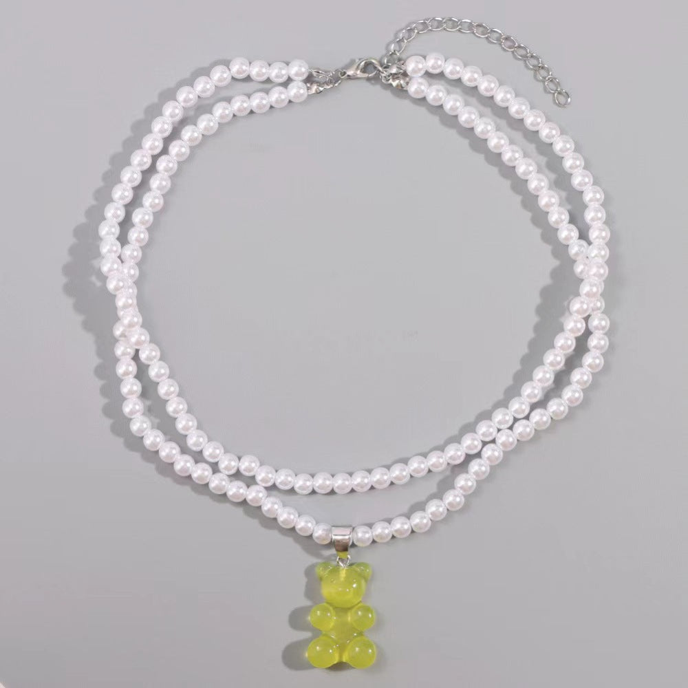 Pearl necklace with yellow teddy bear pendant – trendy layered pearl choker with fun gummy bear charm, statement jewelry on gray background.
