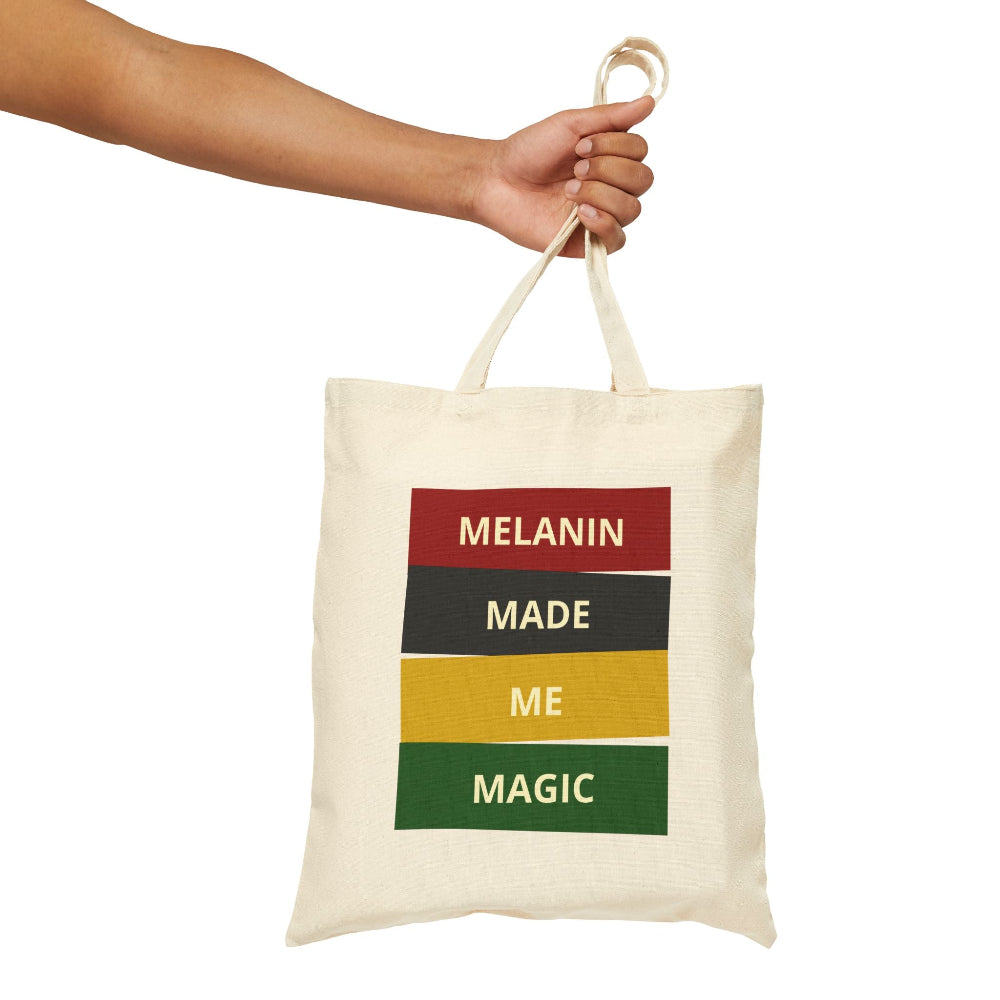 Hand holding natural canvas tote bag with "MELANIN MADE ME MAGIC" graphic.